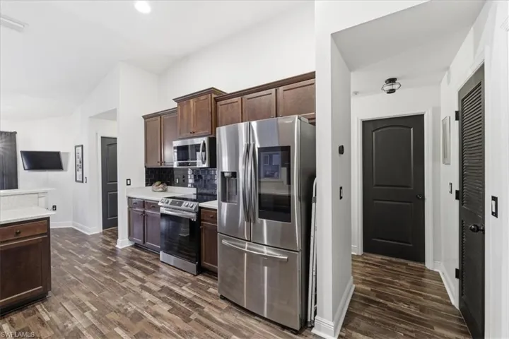 Modern kitchen featuring stainless steel appliances, dark wood cabinetry, light-toned countertops, a dark subway tile backsplash, and wood-finish flooring
