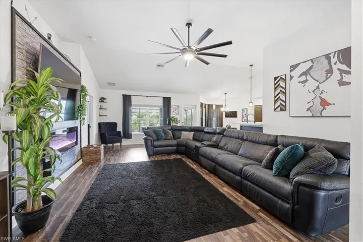 Spacious living area featuring vaulted ceilings with a contemporary ceiling fan, wood-finish flooring, an integrated wall-mounted media console with an electric fireplace, and abundant natural light from multiple windows