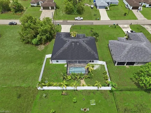 Aerial perspective showcasing a single-story residence with a dark shingle roof and an enclosed swimming pool