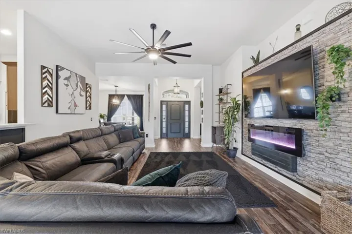 Spacious living area featuring wood-finish flooring, a contemporary ceiling fan, and an accent wall with stone-look paneling