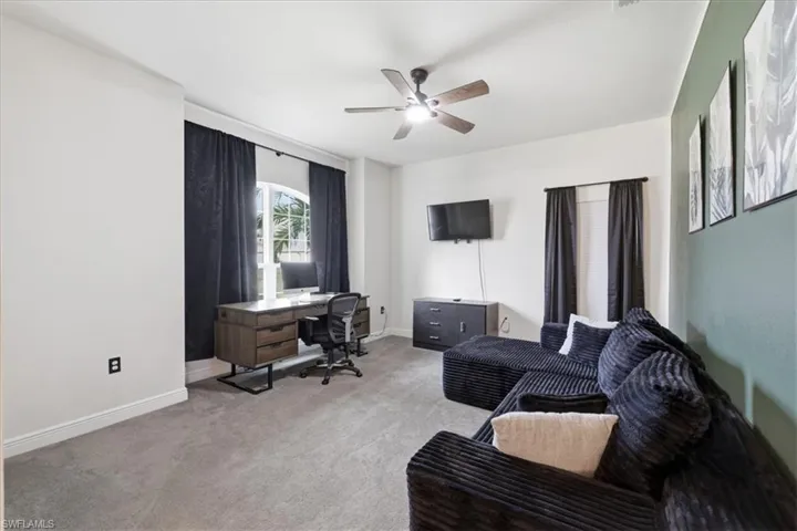 Spacious room featuring light-colored carpeting, a multi-pane arched window, a ceiling fan with light fixture, and contrasting wall colors
