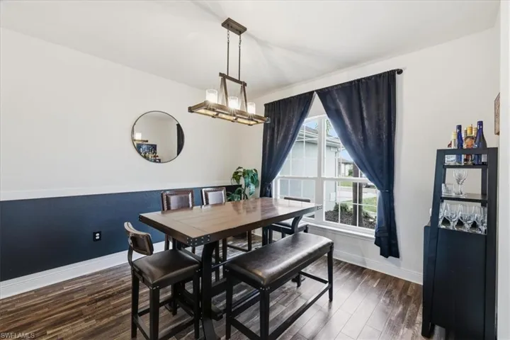 Dining area featuring wood-finish flooring, a contemporary linear chandelier, and a large window with white trim
