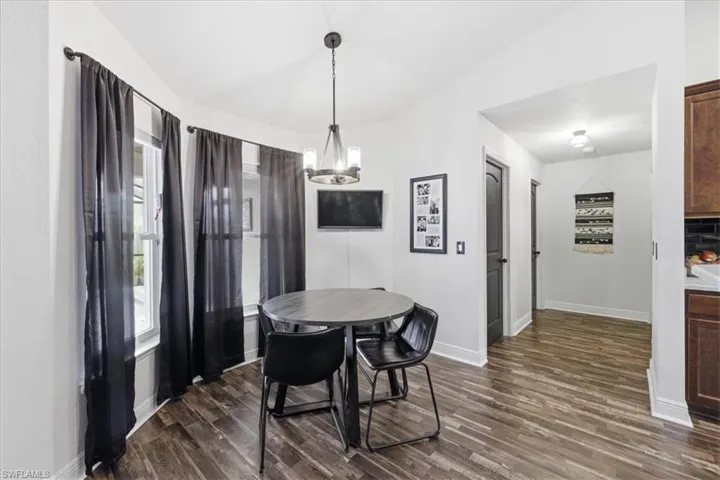 Dining area featuring a contemporary chandelier, large windows with dark drapery, and rich wood-finish flooring