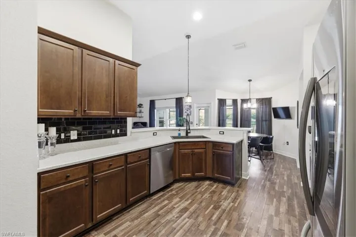 Modern kitchen featuring dark wood cabinetry, light countertops, black subway tile backsplash, stainless steel appliances, and wood-finish flooring