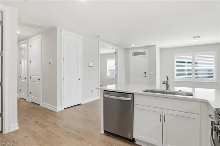 Kitchen with stainless steel appliances, light wood-type flooring, light stone counters, white cabinetry, and recessed lighting