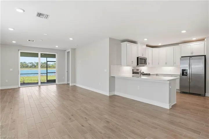 Kitchen featuring stainless steel appliances, white cabinets, open floor plan, light wood-type flooring, and recessed lighting