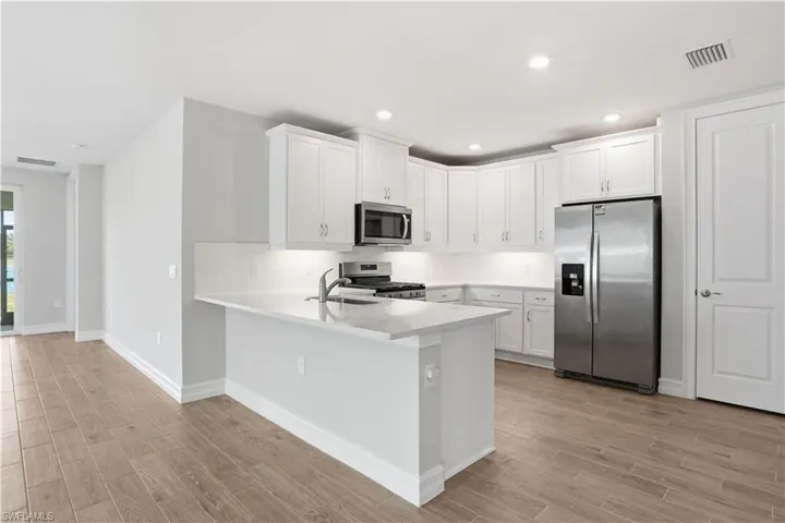 Kitchen featuring stainless steel appliances, white cabinets, wood tiled floors, and recessed lighting