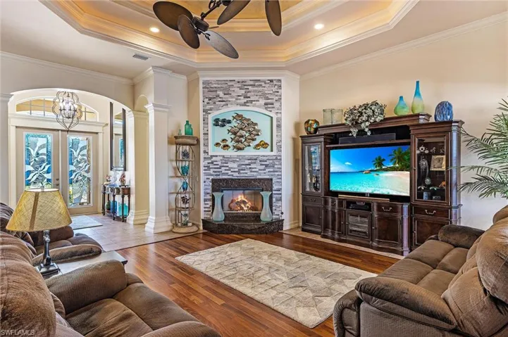 Living area with a raised ceiling, visible vents, a large fireplace, wood finished floors, and ornate columns