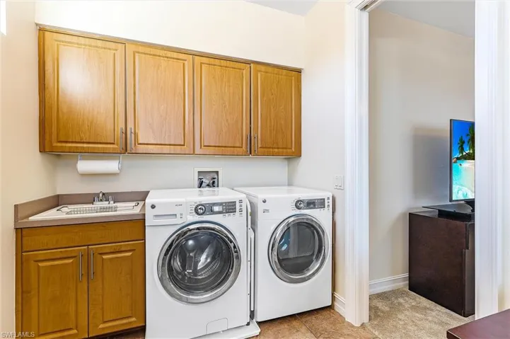 Washroom with cabinet space, light tile patterned floors, baseboards, washing machine and dryer, and a sink