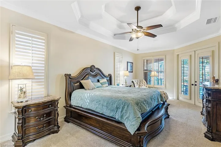 Bedroom with a tray ceiling, light colored carpet, visible vents, ornamental molding, and access to outside