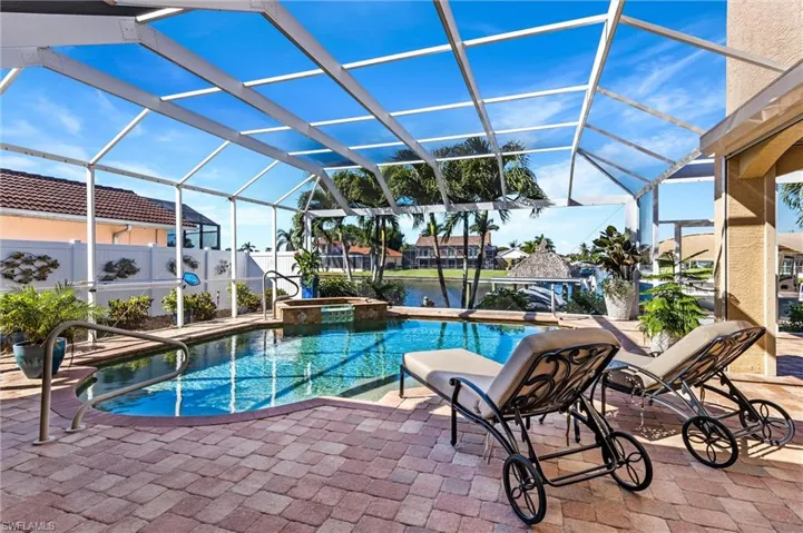 View of pool with a pool with connected hot tub, a water view, a patio area, fence, and a lanai