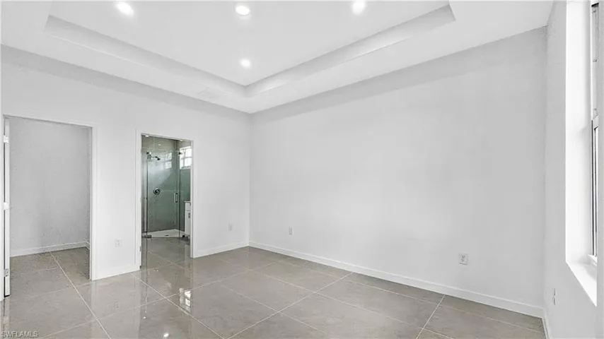 Unfurnished bedroom with a tray ceiling, recessed lighting, light tile patterned floors, and ensuite bathroom
