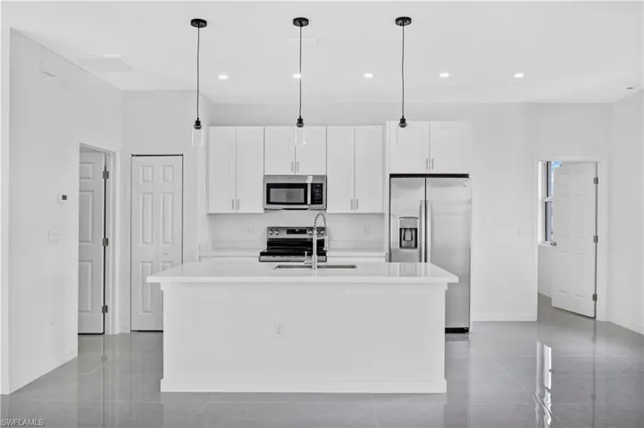 Kitchen featuring stainless steel appliances, white cabinets, an island with sink, light stone countertops, and decorative light fixtures