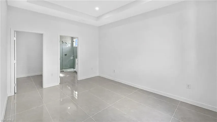 Unfurnished bedroom featuring a raised ceiling, light tile patterned floors, recessed lighting, and ensuite bathroom