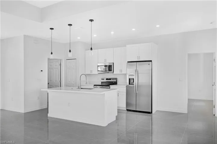 Kitchen featuring stainless steel appliances, white cabinets, a kitchen island with sink, and decorative light fixtures