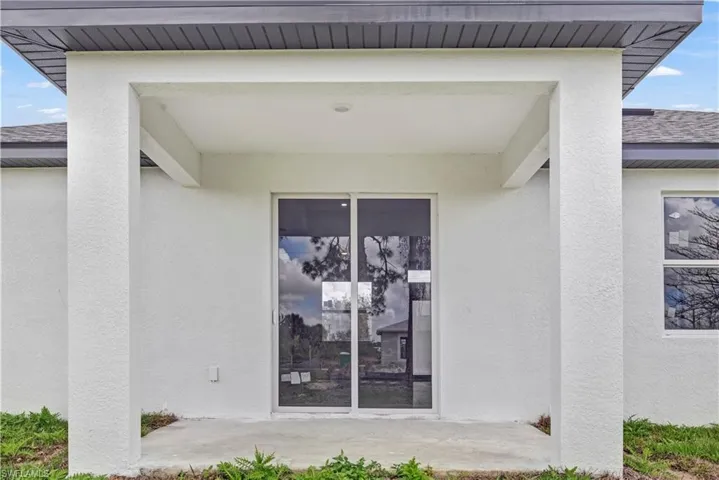 Doorway to property featuring stucco siding, a shingled roof, and a patio