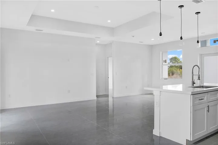 Kitchen featuring hanging light fixtures, light stone counters, open floor plan, an island with sink, and white cabinetry