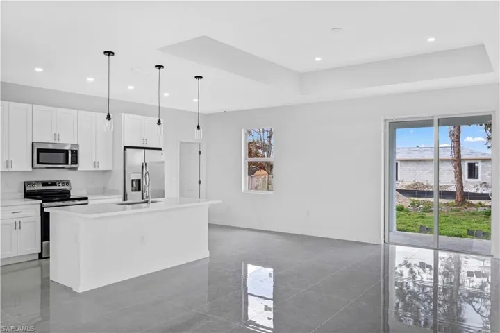 Kitchen featuring stainless steel appliances, white cabinets, plenty of natural light, an island with sink, and a raised ceiling
