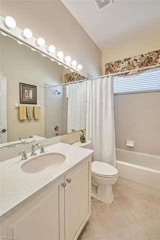 Bathroom with vanity, shower / bathtub combination with curtain, and light tile patterned flooring