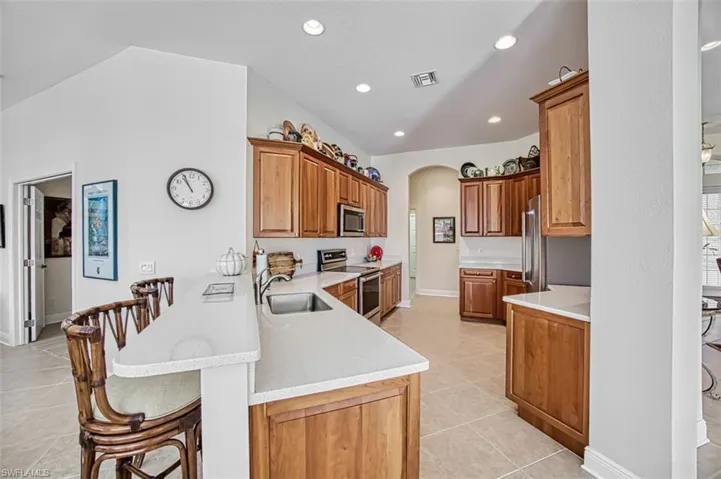 Kitchen featuring a breakfast bar area, arched walkways, brown cabinetry, appliances with stainless steel finishes, and light stone counters
