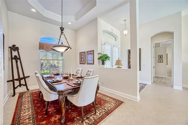 Dining room with ornamental molding, a tray ceiling, arched walkways, light tile patterned floors, and recessed lighting