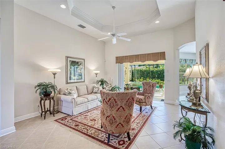 Living room featuring a high ceiling, a tray ceiling, recessed lighting, light tile patterned flooring, and a ceiling fan