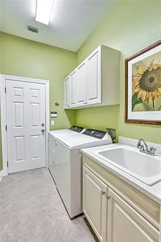Laundry area featuring cabinet space, washing machine and dryer, a textured ceiling, and light tile patterned floors