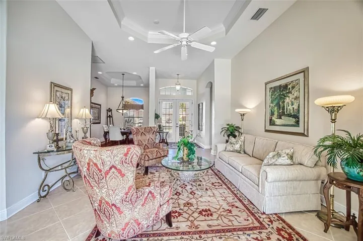 Living area with a tray ceiling, french doors, arched walkways, crown molding, and light tile patterned floors