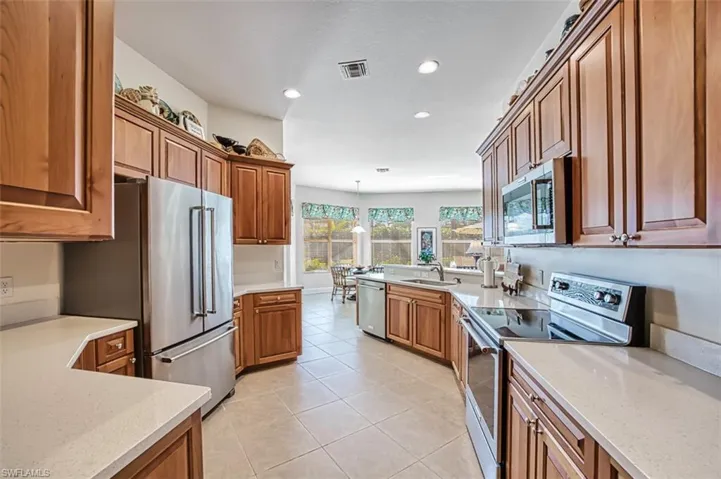 Kitchen featuring appliances with stainless steel finishes, recessed lighting, light tile patterned floors, light stone countertops, and brown cabinets