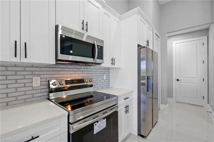 Kitchen featuring stainless steel appliances, white cabinets, decorative backsplash, light stone countertops, and light tile patterned flooring