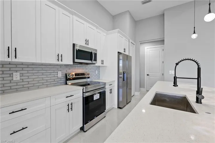 Kitchen with sink, appliances with stainless steel finishes, tasteful backsplash, and light stone counters