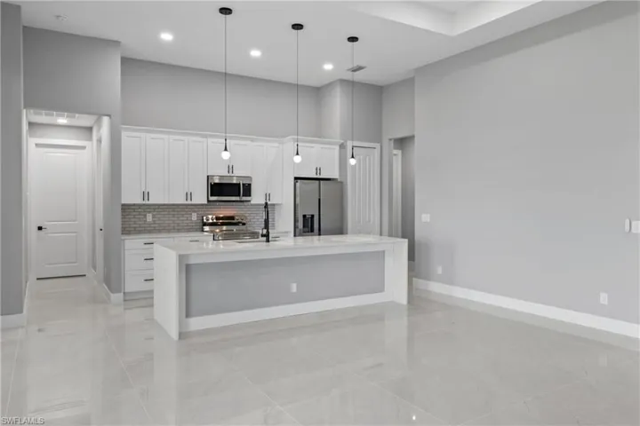 Kitchen featuring appliances with stainless steel finishes, white cabinets, light tile patterned floors, a high ceiling, and an island with sink