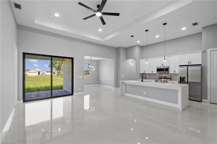 Kitchen featuring sink, appliances with stainless steel finishes, a raised ceiling, and an island with sink