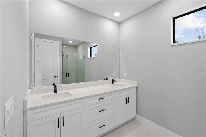 Bathroom featuring dual vanity, tile patterned floors, a shower with door, and plenty of natural light