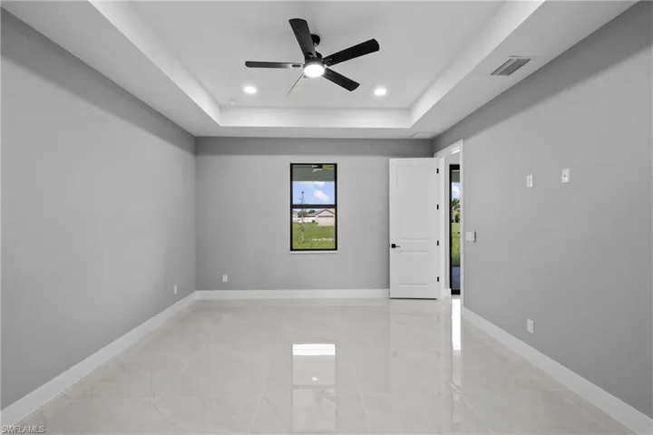 Tiled empty room with ceiling fan and a raised ceiling