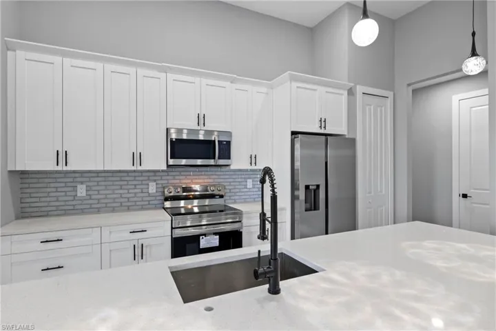 Kitchen with hanging light fixtures, tasteful backsplash, white cabinets, and stainless steel appliances