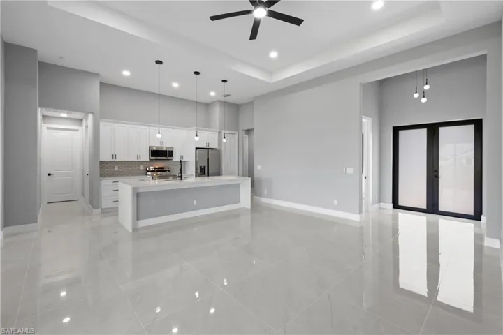 Kitchen featuring light tile patterned flooring, stainless steel appliances, a raised ceiling, and a kitchen island with sink