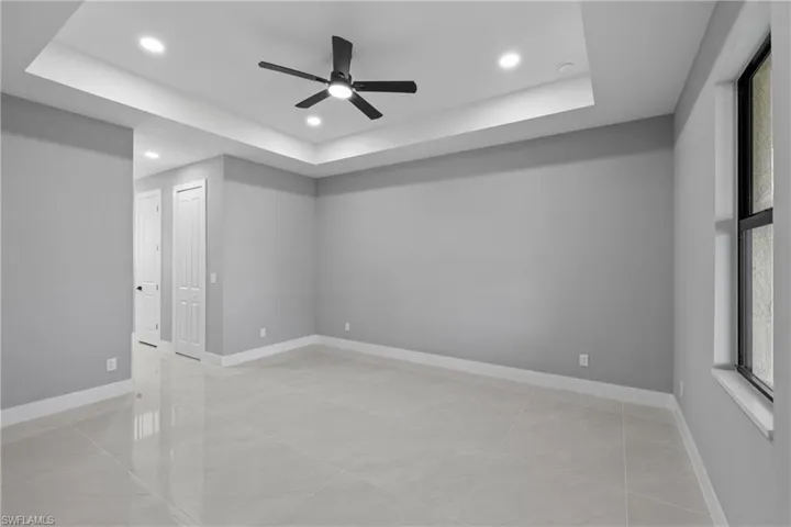 Empty room with ceiling fan, a raised ceiling, and light tile patterned floors