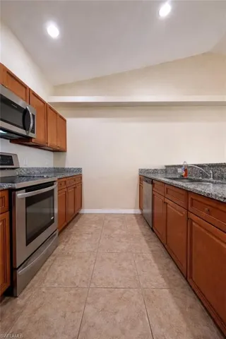 Kitchen featuring appliances with stainless steel finishes, brown cabinets, recessed lighting, and dark stone counters