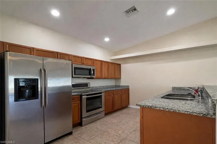 Kitchen with stainless steel appliances, brown cabinetry, dark stone counters, recessed lighting, and light tile patterned floors