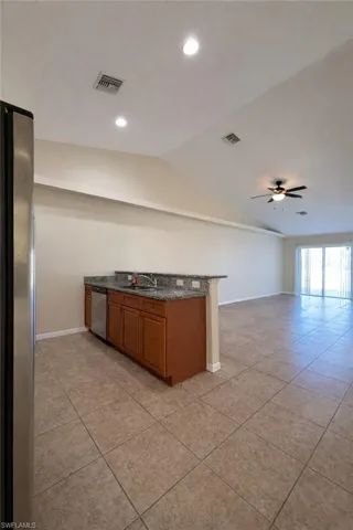 Kitchen with brown cabinetry, dark stone counters, stainless steel appliances, vaulted ceiling, and open floor plan