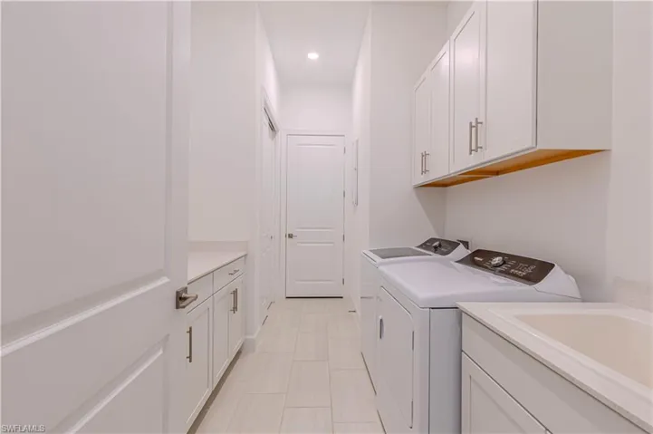 Washroom with recessed lighting, light tile patterned floors, washing machine and clothes dryer, cabinet space, and a sink