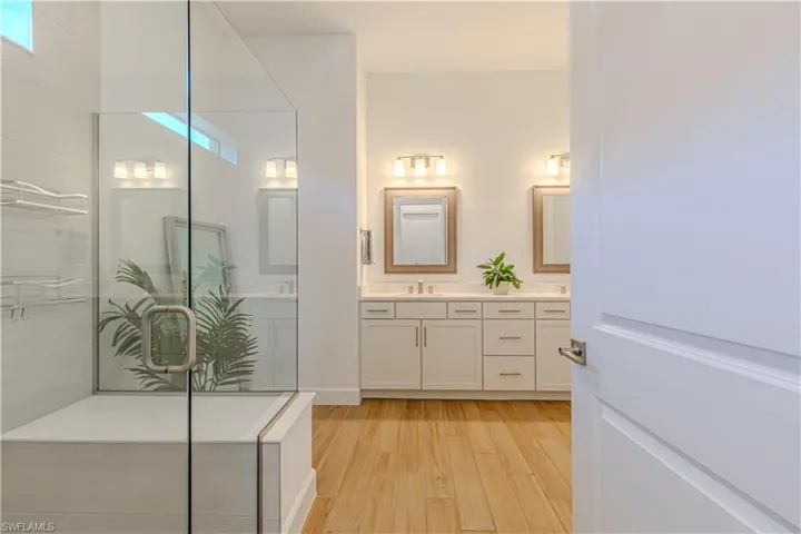 Full bath featuring a sink, a shower with door, double vanity, and wood finished floors