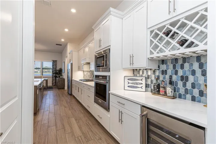 Kitchen featuring white cabinetry, backsplash, stainless steel appliances, beverage cooler, and wood finished floors