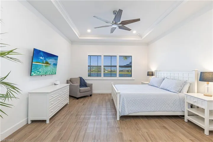 Bedroom featuring baseboards, light wood finished floors, a tray ceiling, and crown molding