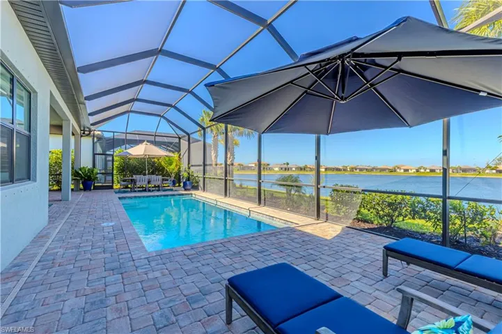 Outdoor pool featuring a patio, a water view, and glass enclosure