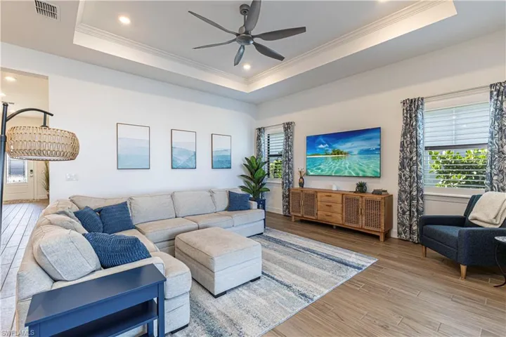 Living area with light wood-type flooring, ornamental molding, a raised ceiling, visible vents, and ceiling fan