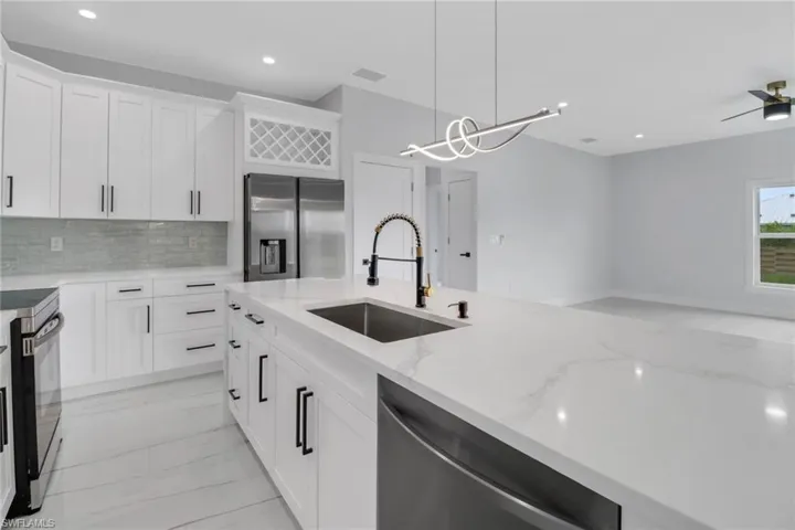 Kitchen with appliances with stainless steel finishes, decorative backsplash, white cabinetry, sink, and ceiling fan