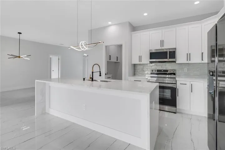 Kitchen with tasteful backsplash, white cabinetry, sink, a center island with sink, and stainless steel appliances