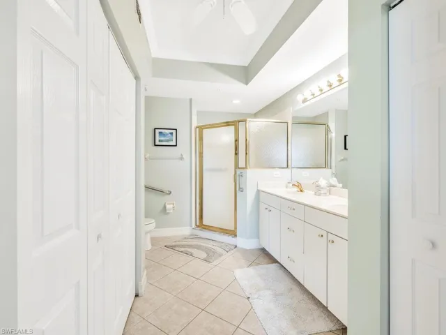 Bathroom with tile  floors, walk in shower, a tray ceiling, dual vanity, and toilet